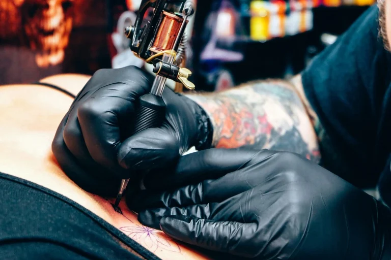 Tatuador tatuando con guantes la piel de un cliente en un estudio de tatuaje profesional en España.